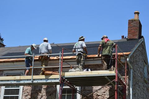 Roofers on scaffolding setting the first course of cedar shakes along a stone house eave