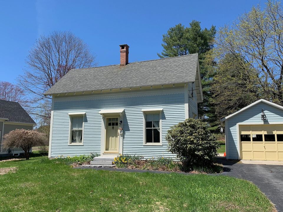 Pale blue New England cape house with a gray shingle roof, chimney and garage