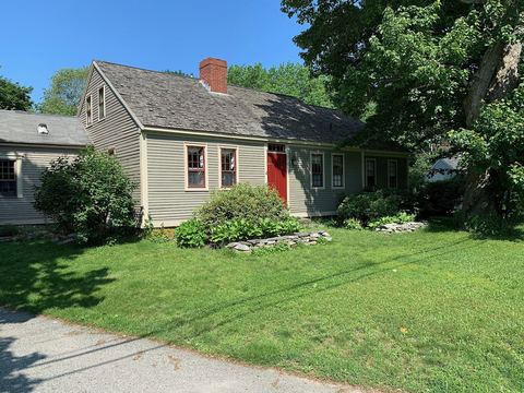 Gray-green New England cape with a weathered cedar shingle roof and a red door