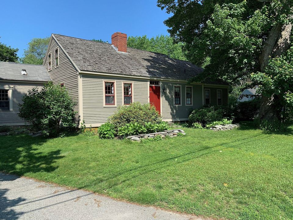 Gray-green New England cape with a weathered cedar shingle roof and a red door