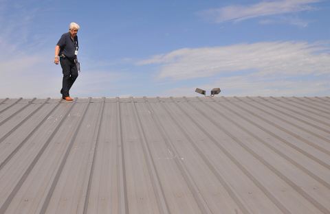 Inspector walking a gray metal roof and checking it for storm damage