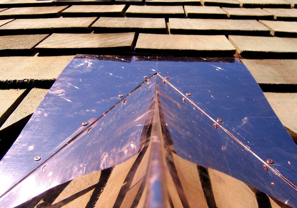 Close-up of new copper ridge flashing nailed over fresh cedar shingles