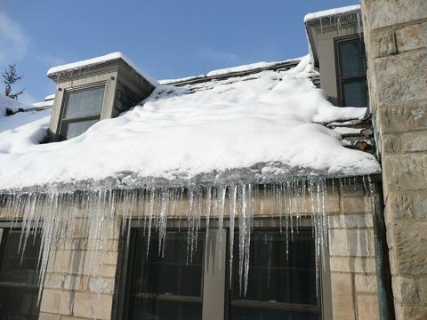 Icicles and an ice dam hanging from a snow-covered slate roof edge